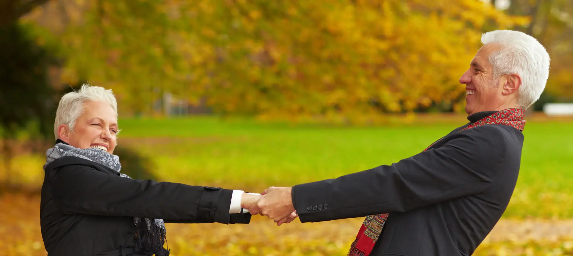 Lachendes Paar mittleren Alters hält sich an den Händen im Park mit buntem Herbstlaub